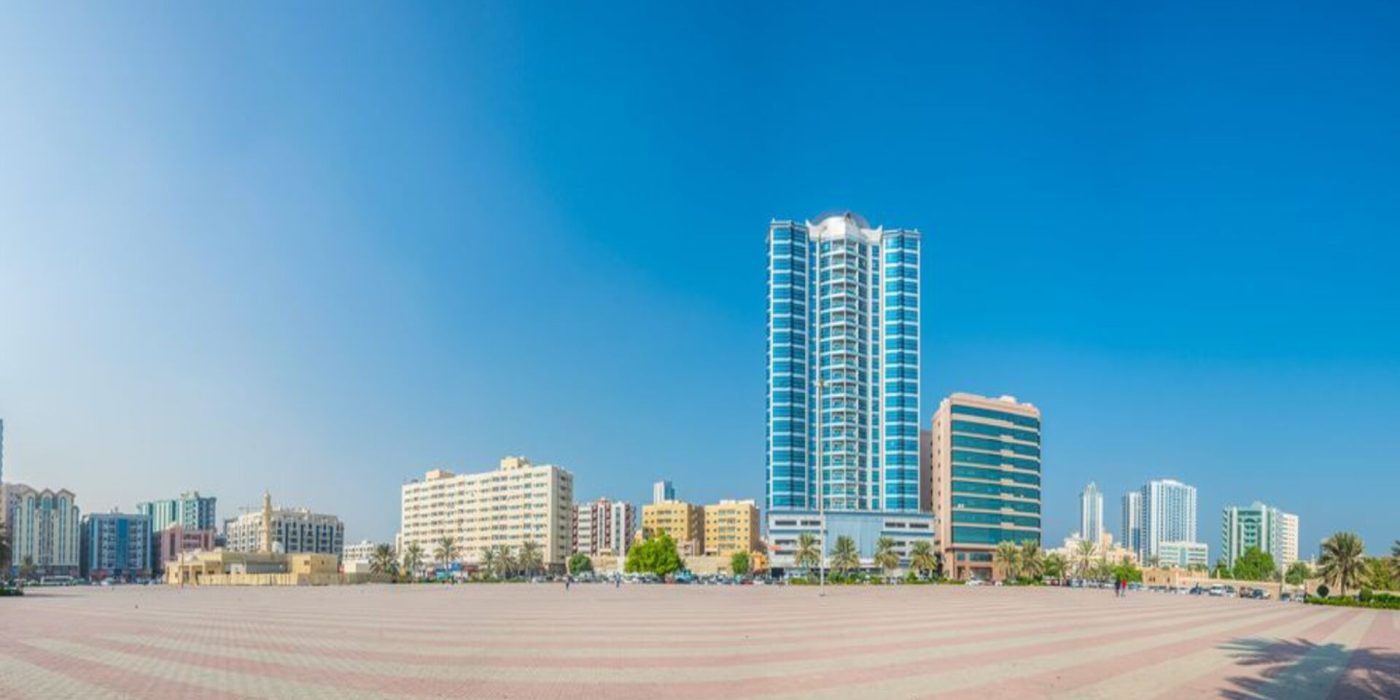 Al Bustan, Ajman skyline with modern buildings and a wide open plaza under a clear blue sky.