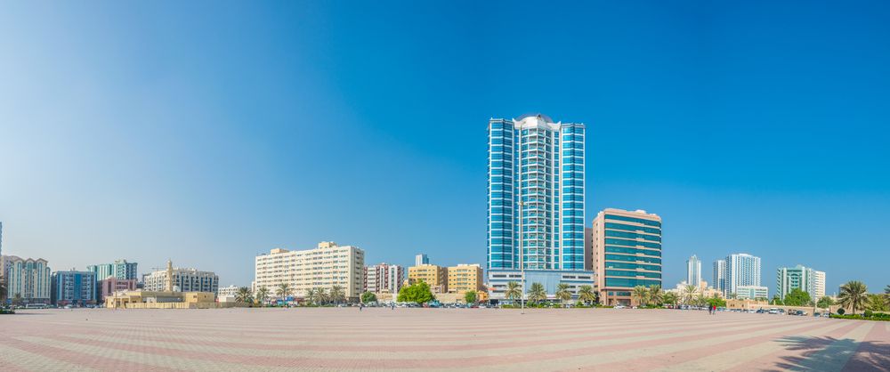 Al Bustan, Ajman skyline with modern buildings and a wide open plaza under a clear blue sky.